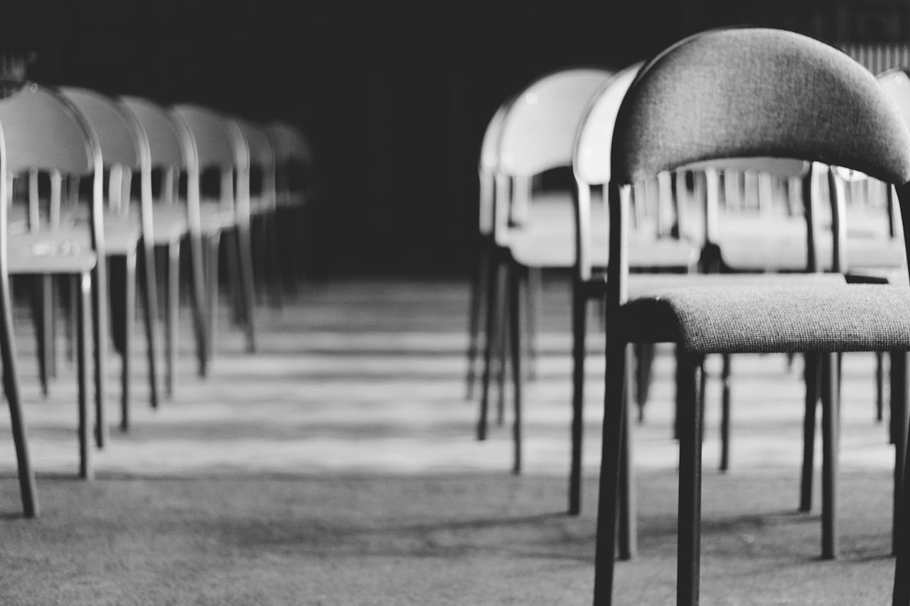 Row of empty chairs in a dimly lit hall, captured in black and white.
