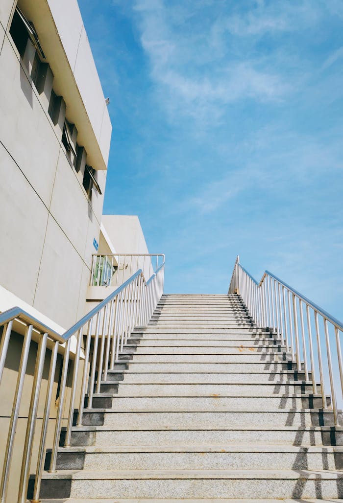 A modern staircase with metal handrails leading up to a blue sky, showcasing urban architecture.
