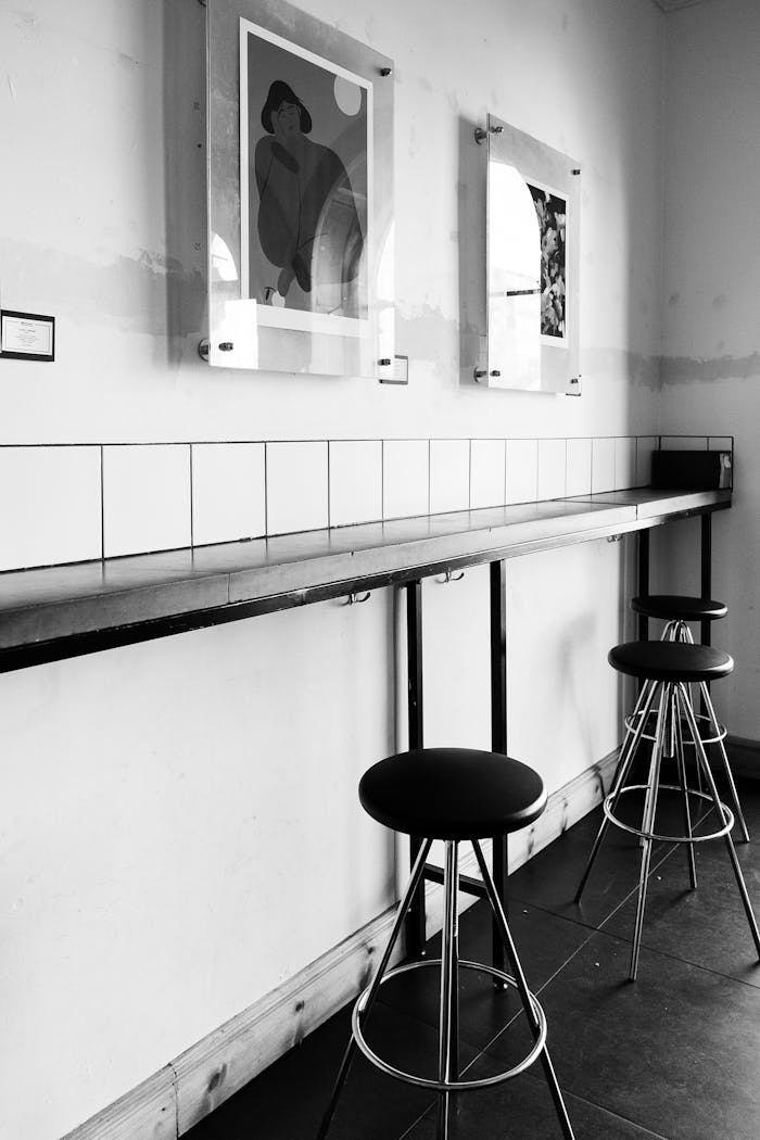 Black and white photo of an empty café interior with stools and wall art.