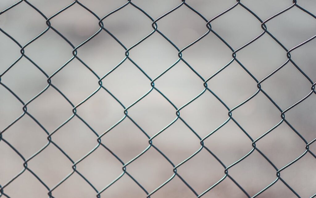 pexels-photo-683402 Detailed closeup of a metal chain-link fence with a blurred neutral background, perfect for textures and overlays.